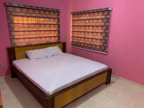 a bed in a bedroom with pink walls and windows at New Bungalow 2 Bed House in Adewumi, Off Olodo rd Ibadan in Ibadan