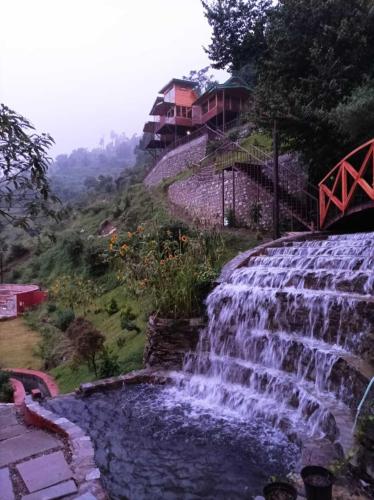 a waterfall on the side of a hill with houses at Atulyam, Pangot in Nainital