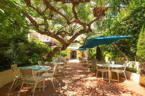 un patio con mesas, sillas y una sombrilla en Hôtel Jardin Croisette, en Cannes