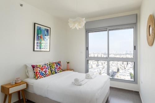 um quarto branco com uma cama e uma grande janela em Deluxe & Terrace with City Overview by FeelHome em Holon