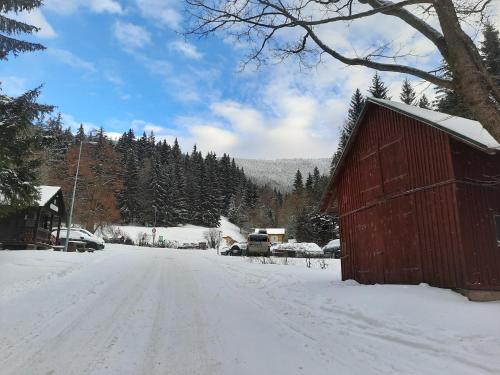 a snow covered road with a red barn on the side at Velký apartmán Cihlarka in Cerny Dul