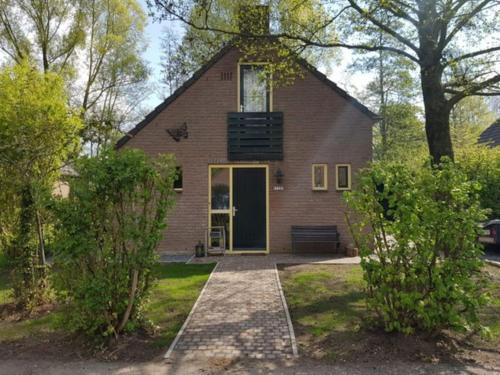 a brick house with a yellow door and trees at De Zingende Wilg, heerlijk huisje met Hottub in Ewijk