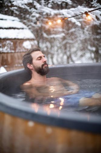 a man in a hot tub in a snow covered yard at DAS SCHÖNE LEBEN Pop-Up Hotel in Hornberg
