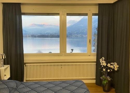een slaapkamer met een groot raam met uitzicht op het water bij Alloggio con favolosa vista lago Lugano Paradiso in Paradiso