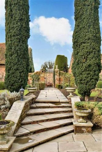 a stone walkway in a garden with two trees at B&B Harlington Manor in Harlington