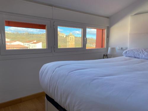 um quarto com uma cama branca e 2 janelas em Vivienda turística Los Tejados em Soria