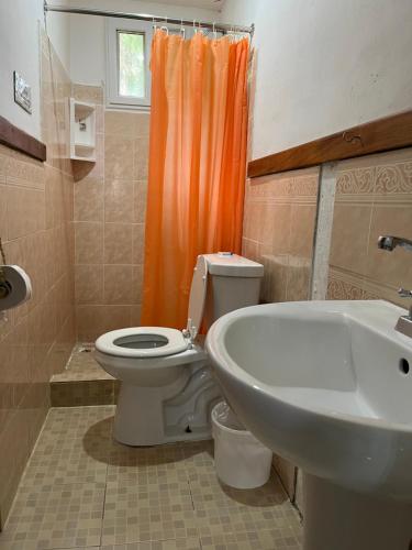 a bathroom with a toilet and an orange shower curtain at A&K Island Apartments in Bocas Town