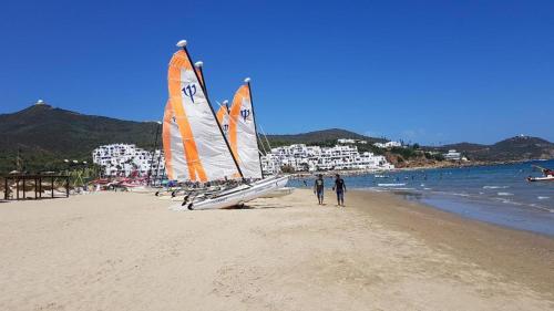 two people walking on a beach with two sailboats at la Cassia Cabo Appartement in Cabo Negro