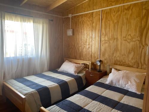two beds in a small room with a window at Cabañas y Tinajas Rio Quenuir in Maullín