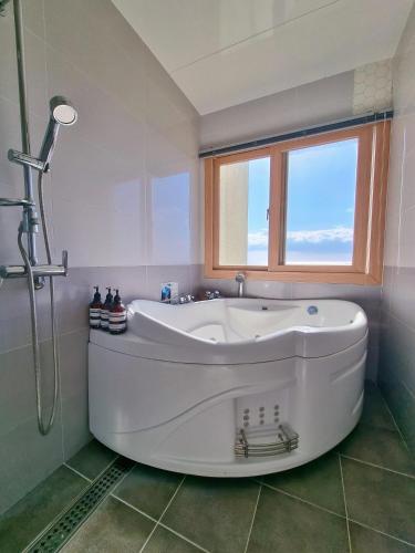 a white tub in a bathroom with a window at Jeju the Ocean Hill Pension in Seogwipo