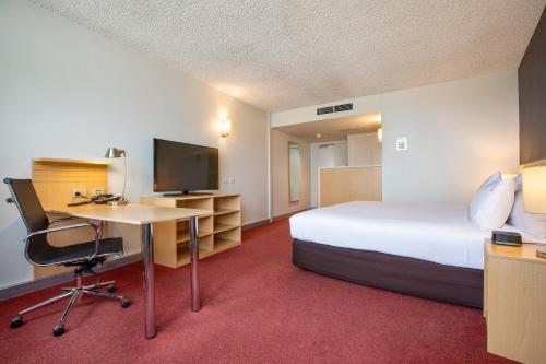 a hotel room with a bed and a desk with a computer at Holiday Inn Melbourne Airport by IHG in Melbourne