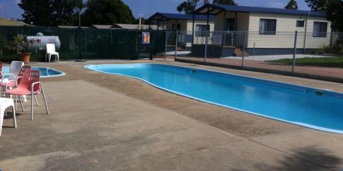 a swimming pool in a yard with chairs and a house at Lakes Entrance Tourist Park in Lakes Entrance