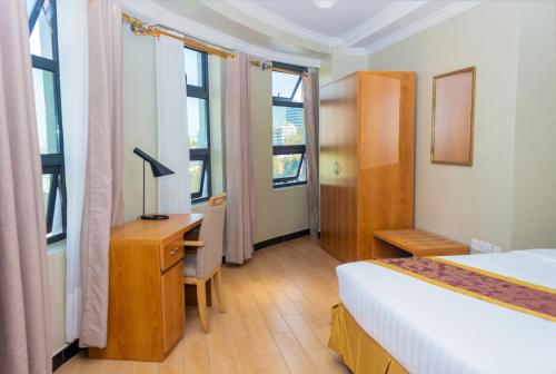 a bedroom with a bed and a desk and windows at Tropical Plaza Apartments in Kigali