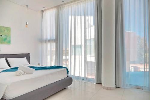 a white bedroom with a bed and large windows at Sunrise Seaview Villas - Camelia in Paralimni
