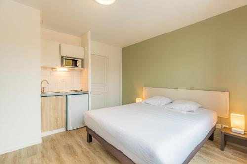 a bedroom with a large white bed and a kitchen at Appart'City Classic Bourg-en-Bresse in Bourg-en-Bresse