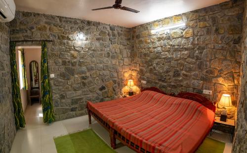 ein Schlafzimmer mit einem roten Bett in einer Steinmauer in der Unterkunft Bamboo Banks Farm & Guest House in Masinagudi