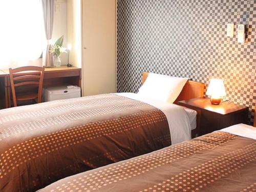 a bedroom with two beds and a table with a lamp at HOTEL LiVEMAX BUDGET Tokyo Hamura Ekimae in Hamura