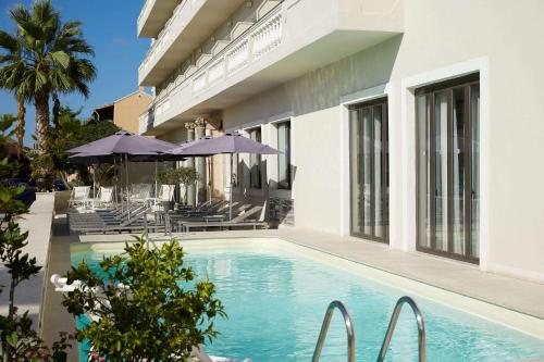 a swimming pool with chairs and umbrellas next to a building at Mon Repos Palace - Adults Only in Corfu