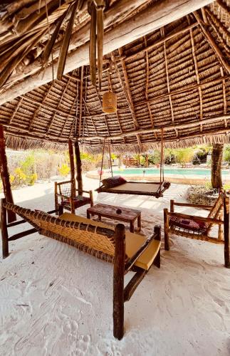 a beach with chairs and a straw umbrella and swings at Mpole Bungalows in Michamvi