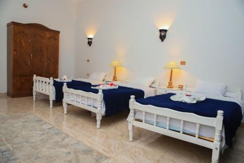 Luxor Oasis Guest House في الأقصر: غرفة نوم بثلاث اسرة وطاولتين ومصبغتين