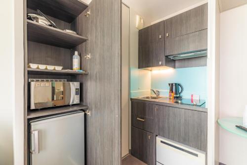 a kitchen with dark wood cabinets and a microwave at Appart'City Confort Montpellier Ovalie II in Montpellier