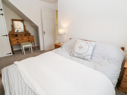 a bedroom with a white bed and a dresser and a mirror at Primrose in Holsworthy