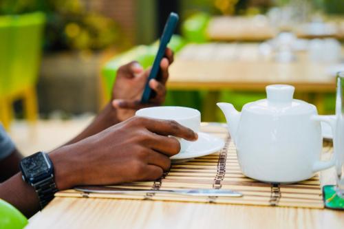 a person sitting at a table with a cup and a cell phone at J leaf Hotel by Blue Bird in Negombo