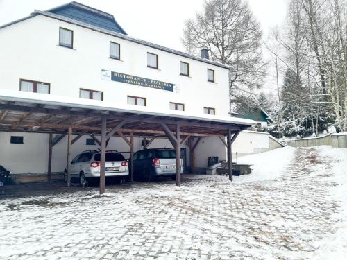 two cars parked in front of a building in the snow at Pizzeria Pension Damiano in Muldenhammer