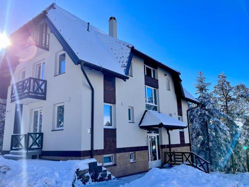 a house covered in snow with the sun behind it at Apartmani Divila in Divčibare