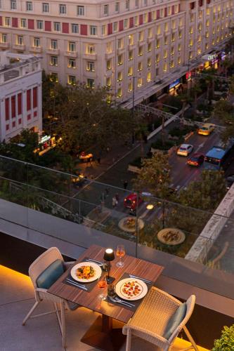 a table and chairs on a balcony with a view of a city at Athens Capital Center Hotel - MGallery Collection in Athens