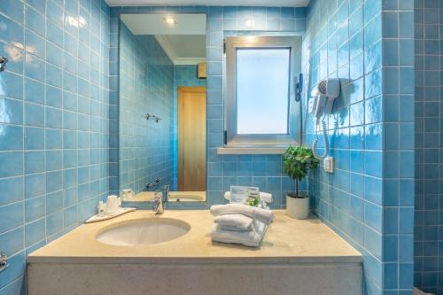 baño de azulejos azules con lavabo y ventana en Pontalaia Apartamentos Turísticos, en Sagres