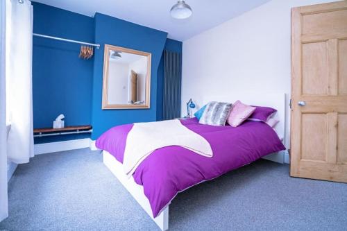 a bedroom with blue walls and a bed with purple sheets at Quaint house in a beautiful rural setting in Froghall