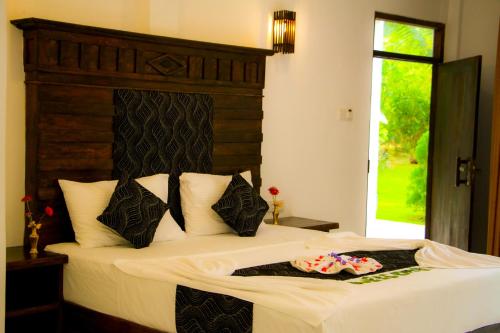 a bedroom with a large bed with white sheets and black pillows at Manike Lodge Habarana in Habarana