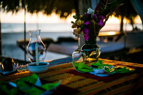 a table with two wine glasses and a vase with flowers at Hotel El Copal in Mazunte