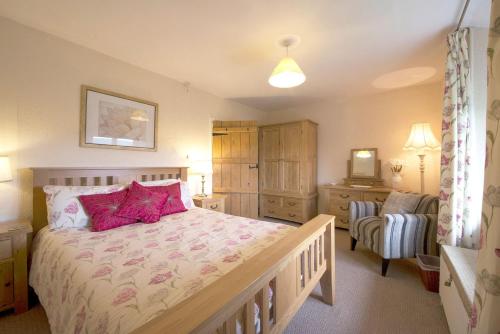 a bedroom with a bed with pink pillows and a chair at Old Quarry Cottage Coniston in Coniston