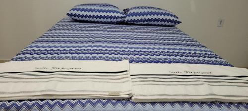 a bed with blue and white striped sheets and pillows at Suite Pajuçara in Maceió