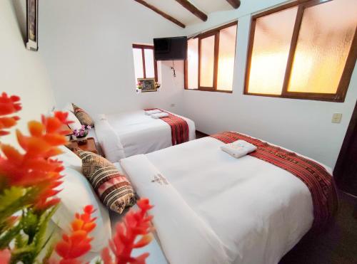 two beds in a room with windows and flowers at House Cusco in Cusco