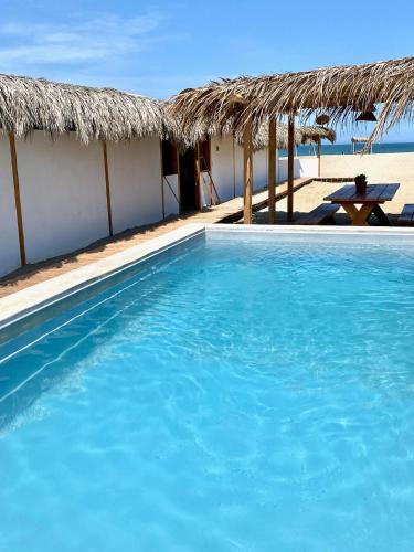 a swimming pool next to a resort with a thatch roof at Vistazul in Vichayito
