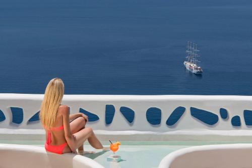 a woman sitting on a ledge looking out at the ocean at Athina Luxury Suites in Fira