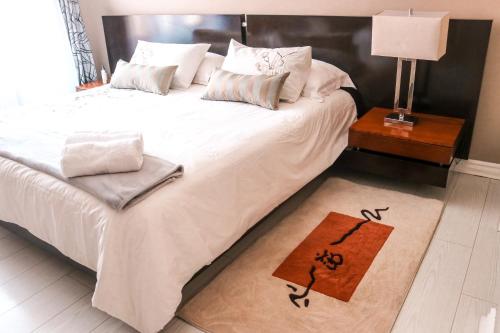 a bedroom with a bed with white sheets and a table with a lamp at Modern Home in Pretoria near Menlyn Mall in Pretoria