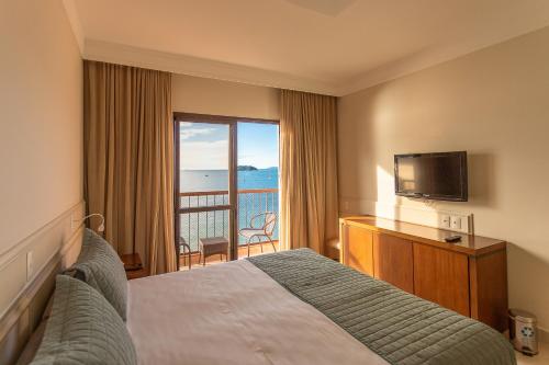 a hotel room with a bed and a television and a balcony at Hotel Jurerê Beach Village - OFICIAL in Florianópolis