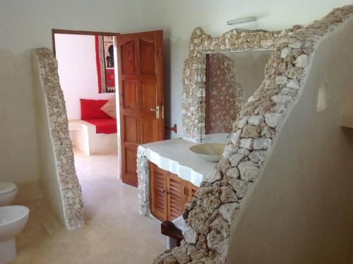 baño con pared de piedra con lavabo y espejo en Luxury Simba House in Watamu [ ☆☆☆☆☆ ] en Watamu