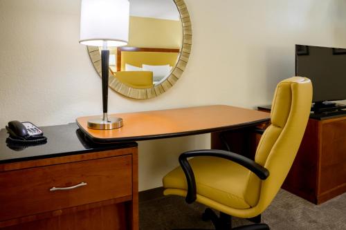 a desk with a yellow chair and a mirror at Airtel Plaza Hotel in Van Nuys