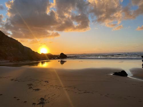 a sunset on a beach with footprints in the sand at Herdade AMÁLIA RODRIGUES in Zambujeira do Mar