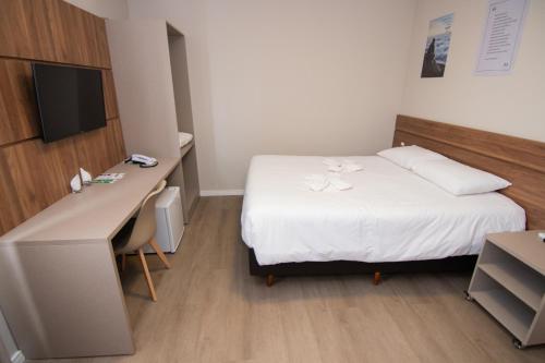een kamer met een bed, een bureau en een televisie bij Hotel Maua in Curitiba
