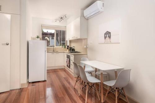 a kitchen with a table and chairs and a white refrigerator at Bright & Comfy 2 Bedroom St Kilda East Apartment in Melbourne