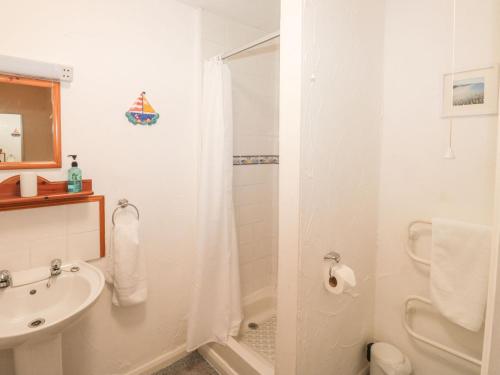 un bagno bianco con doccia e lavandino di Bluebell Cottage a Paignton