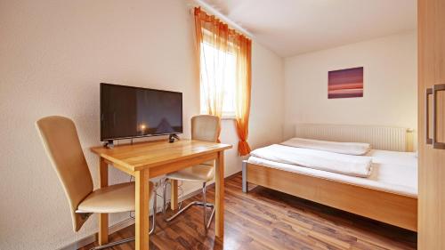 um quarto com uma secretária, uma cama e uma televisão em Fleiner Gästehaus em Flein