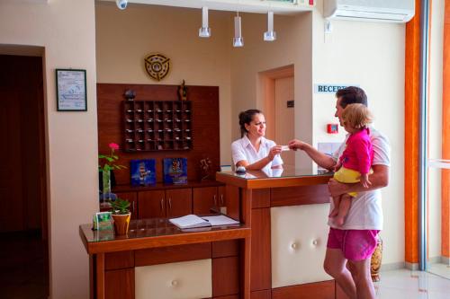 a man and a woman standing at a counter with a little girl at Hotel Loukas Vrachos in Paralia Vrachou