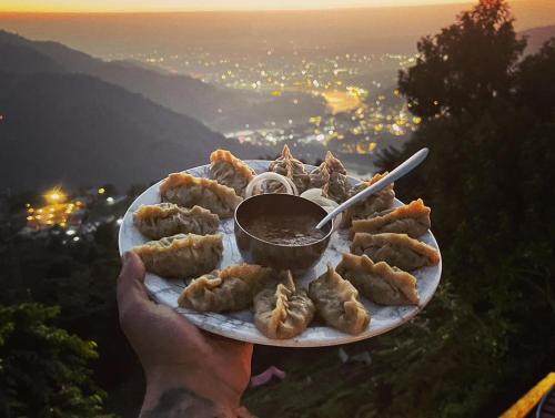 Wild Mountain Homestay في ريشيكيش: شخص يحمل طبق من الطعام مع الغطس